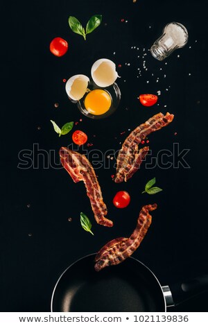 Foto stock: Close Up View Of Raw Egg Yolk And Salt Falling On Frying Pan Isolated On Black