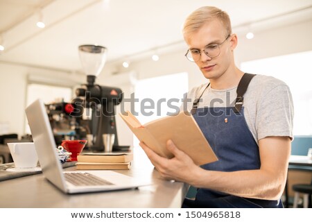 Stok fotoğraf: Young Confident Barista Or Waiter Of Restaurant Reading Book Or Manual