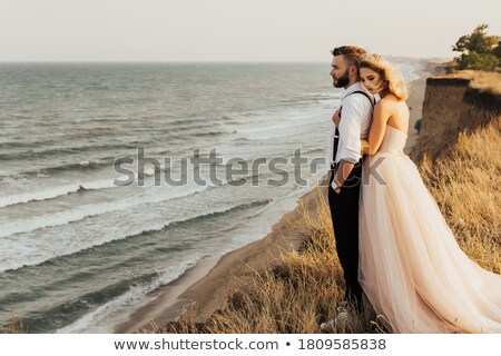 ストックフォト: Newlyweds In Love Stand On The Nature Against The Background Of Wooden Stakes In Sunny Weather St