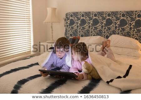Foto stock: Front View Of Sweet Brother And Sister Using Digital Tablet Under Blanket In Bedroom At Home