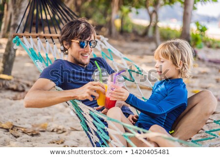 Foto d'archivio: Dad And Son Having Fun In A Hammock With A Drinks