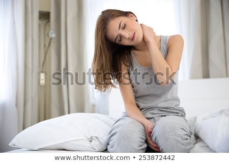 Stockfoto: Young Woman Sitting On The Bed With Pain In Neck