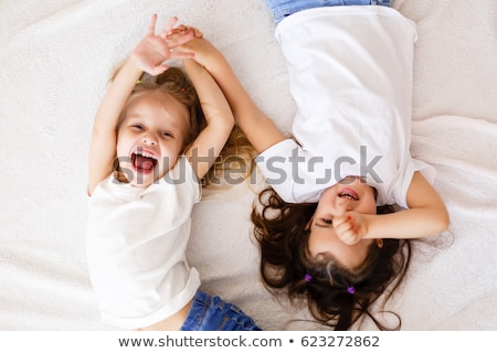 Сток-фото: Two Cheerful Laughing Girls In White Shirts On Bed