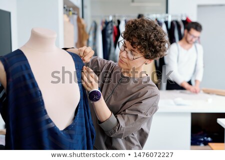 Young Serious Seamstress Stitching Unfinished Blue Dress On Mannequin Foto stock © Pressmaster