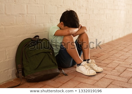 Сток-фото: Side View Of A Sad Caucasian Schoolboy Sitting Alone On Floor In The Locker Room At School