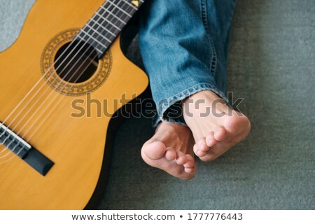 Stock photo: Barefoot Guitarist With Legs Outstretch Beside Guitar