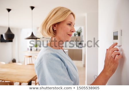 ストックフォト: Woman Adjusting Thermostat On Central Heating Control