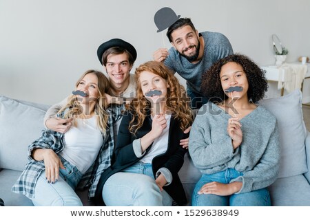 Stock photo: Three Funny Girls With Moustaches Sitting On Couch With Two Happy Guys Behind