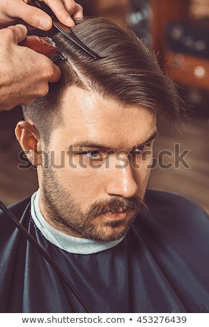 Stock photo: The Hands Of Young Barber Making Haircut To Attractive Man In Ba