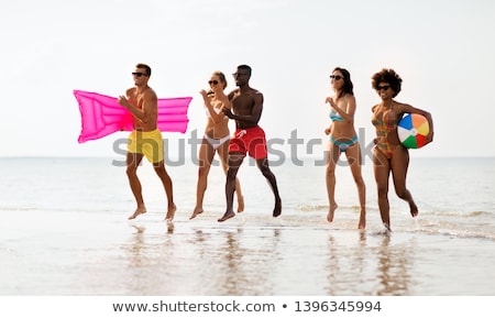 Foto stock: Friends Run With Beach Ball And Swimming Mattress