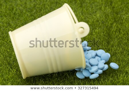 Foto stock: Blue Pills Spilled From A White Bucket On The Green Grass