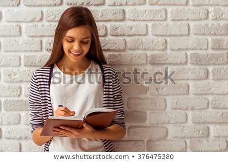 Stok fotoğraf: Smiling Girl Writing On A Notebook Against A White Background