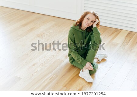 Stockfoto: Pleased Restful Woman Has Gentle Smile Makeup Wears Sportswear White Sneakers Poses On Laminate