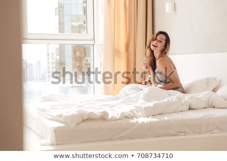 Foto stock: Cheerful Pretty Young Woman Sitting In Bed And Holding Pillow