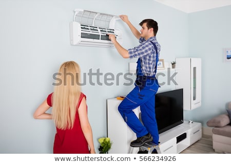 Stockfoto: Woman Looking At Technician Repairing Air Conditioner