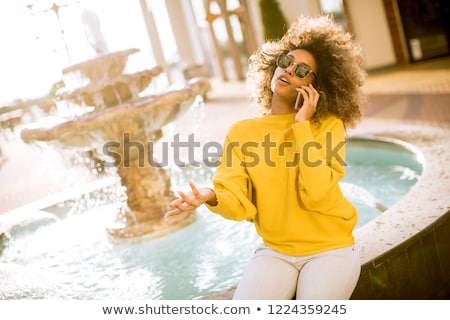 Foto stock: Aftican American Young Woman Sits Near Fountain And Talks On Mob