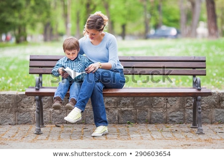 Foto stock: Adre · con · hijos · sentarse · en · un · banco · y · leer · un · libro