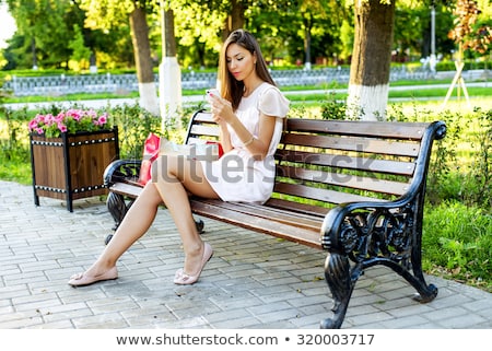 Foto stock: Cheerful Young Girl Sitting On A Bench At The Park