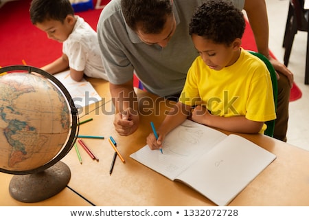 [[stock_photo]]: High Angle View Of A Handsome Caucasian Male Teacher Teaching A Mixed Race Schoolboy In A Classroom