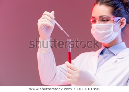 Zdjęcia stock: Young Chemist In Protective Eyeglasses And Mask Dropping Red Fluid Into Flask