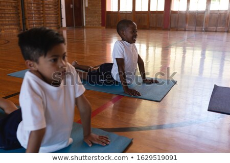 Foto stock: Side View Of Schoolkids Doing Yoga Position On A Yoga Mat In School Gymnasium