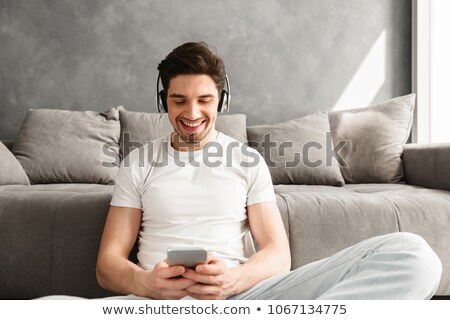 Сток-фото: Cheerful Man 30s In White T Shirt Sitting On Floor Indoor And L