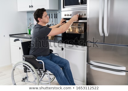 Foto stock: Disabled Man Using Microwave Oven In Kitchen