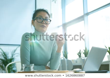 Foto stock: Young Asian Female Looking At You While Having Cup Of Tea Or Coffee By Table