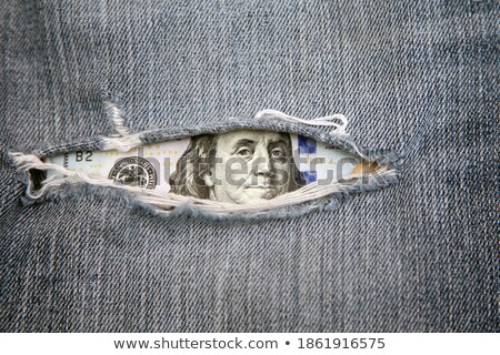 Stock foto: Hundred Dollars Bill Through Torn Blue Jeans Texture