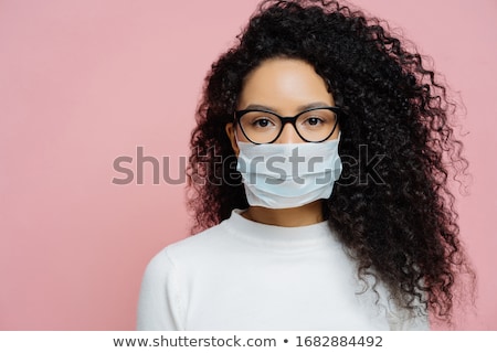 Stockfoto: Image Of Serious Curly Haired Young Woman Wears Medical Mask Keeps Thumb Down Shows Dislike Gestur