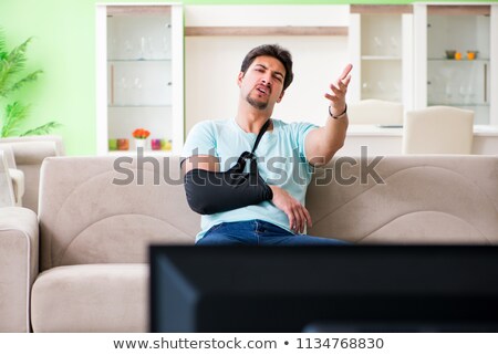 Stockfoto: Arm Injured Man Sitting On The Sofa Watching Tv