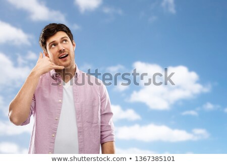 Stockfoto: Young Man Showing Phone Call Gesture Over Blue Sky
