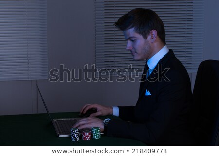 [[stock_photo]]: Businessman Working Late On Laptop By Stacked Poker Chips