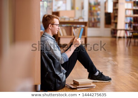 ストックフォト: Clever Guy In Denim Shirt And Black Jeans Reading By Bookshelf