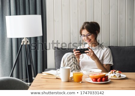 Stockfoto: Photo Of Woman Playing Video Game On Cellphone While Having Breakfast