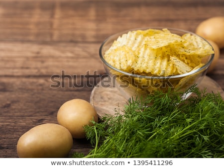 Stock fotó: Homemade Potato Crisp Chips Inside Glass Bowl With Fresh Raw Dill On Wooden Background And Raw Potat