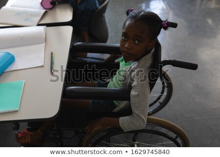 Stock photo: High Angle View Of Disable Schoolgirl Looking At Camera And Raising Hand In Classroom Of Elementary