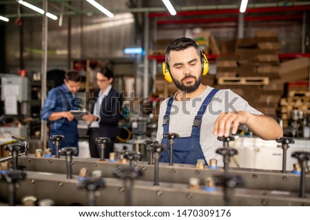 Young Bearded Mechanic In Protective Headphones Repairing Industrial Machine 商業照片 © Pressmaster