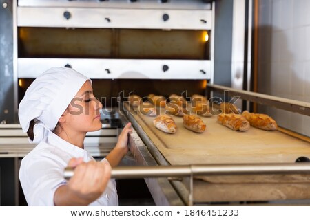 Foto stock: Baker Pulling A Freshly Baked Baguette Out From The Oven