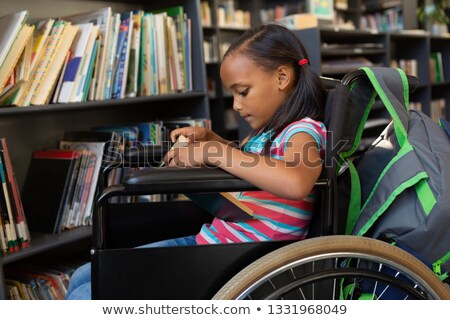 Foto d'archivio: Side View Of A Cute Disabled Mixed Race Schoolgirl Reading A Book In The Classroom At School