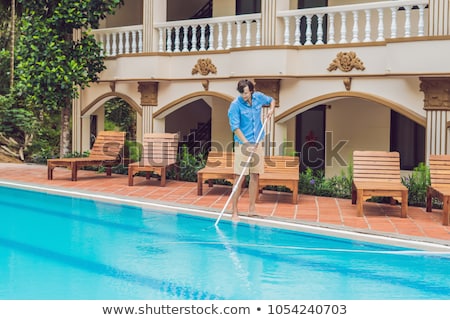 Сток-фото: Cleaner Of The Swimming Pool Man In A Blue Shirt With Cleaning Equipment For Swimming Pools Sunny
