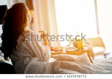 ストックフォト: Smiling Woman Drinking A Coffee Lying On A Bed At Home Or Hotel