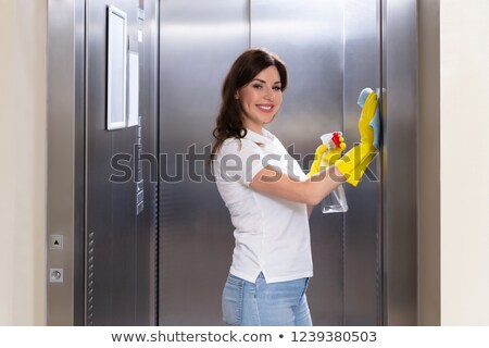 [[stock_photo]]: Female Janitor Cleaning Elevator With Duster