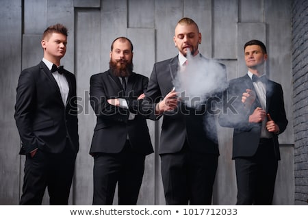 Stok fotoğraf: Elegant Young Businessman Standing And Smoking In Studio