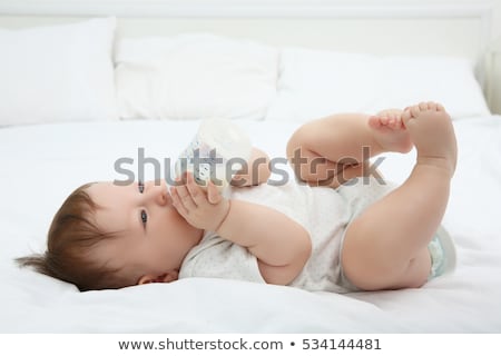 Foto stock: Little Child Girl Lying On White Bed And Drinking Milk From Bottle