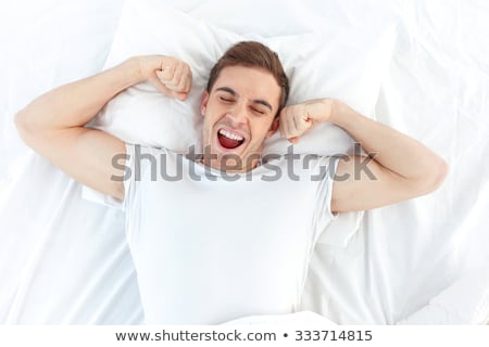 Stock photo: Cheerful Young Man Waking Up In Bed And Stretching His Arms
