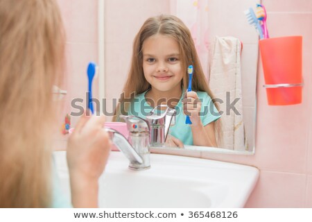 Stock photo: Six Year Old Girl Holding A Toothbrush And Looks At Himself In The Mirror While In The Bathroom