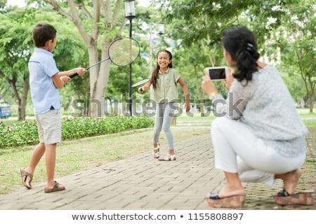 Foto stock: Mother Taking Picture Of Kids Playing Badminton