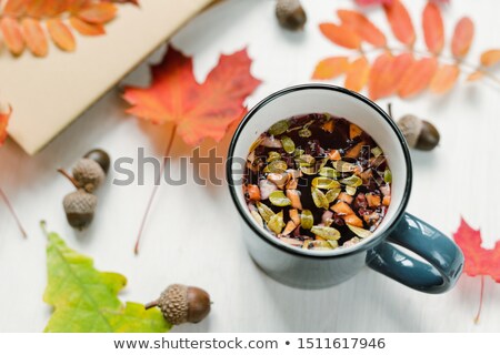 Stockfoto: Mug With Hot Black Herbal Tea On Table With Acorns And Mixture Of Red Leaves