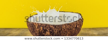 Stok fotoğraf: Coconut Fruit And Milk Splash Inside It On Yellow Background Banner Long Format